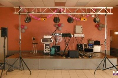 Matériel de sonorisation et éclairage installé sur une petite scène dans une salle avec décoration simple.