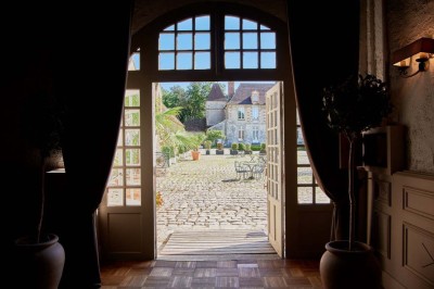 Cour pavée avec des tables en fer forgé, devant une bâtisse en pierre éclairée par des lumières chaudes.
