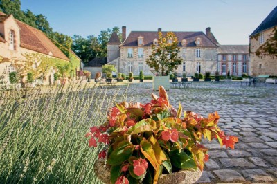 Cour pavée avec des tables en fer forgé, devant une bâtisse en pierre éclairée par des lumières chaudes.