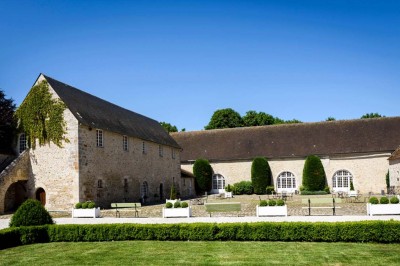 Cour pavée avec des tables en fer forgé, devant une bâtisse en pierre éclairée par des lumières chaudes.