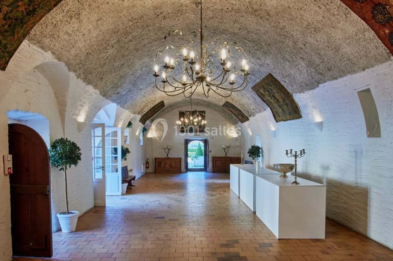 Salle voûtée avec murs en pierre blanche, lustres suspendus, décorations murales et mobilier minimaliste.