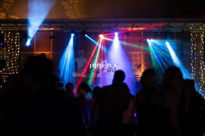 Personnes dansant devant une scène illuminée par des projecteurs colorés lors d'une soirée en plein air.