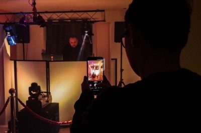 Une personne filme un DJ en pleine performance dans une salle éclairée par des lumières de scène.