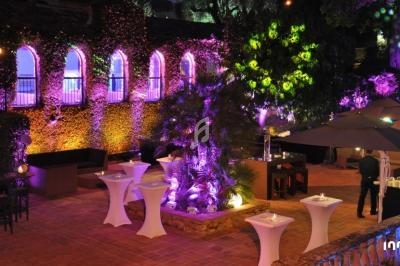 Terrasse éclairée en soirée avec des tables hautes, des parasols et une façade végétalisée illuminée.