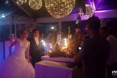 Un couple de mariés pose près d'une table décorée avec des desserts et des fontaines lumineuses sous un éclairage tamisé.