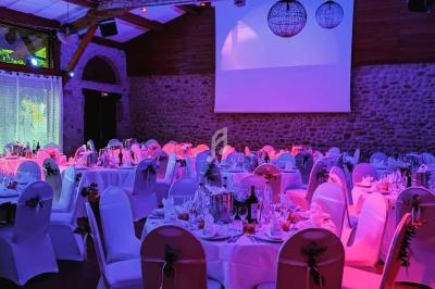 Salle de réception décorée avec des tables rondes dressées, éclairage coloré et projecteurs au plafond.