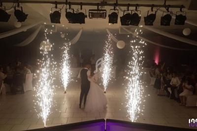 Un couple danse au centre d'une salle décorée, entouré de jets d'étincelles et d'invités assis.