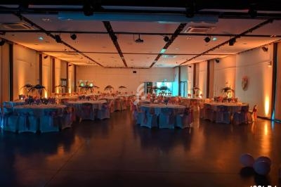 Salle de réception décorée avec des tables rondes, nappes blanches et éclairage tamisé orangé.