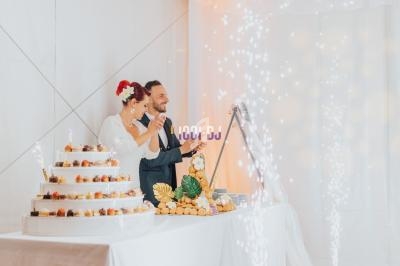 Un couple coupe un gâteau de mariage à plusieurs étages dans une salle décorée avec des lumières scintillantes.