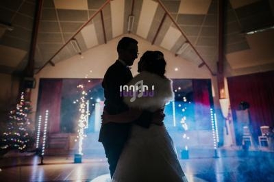 Un couple danse dans une salle décorée avec des lumières et de la fumée, ambiance festive et tamisée.
