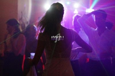 Une femme en robe blanche danse sous des lumières colorées dans une ambiance festive avec d'autres personnes.