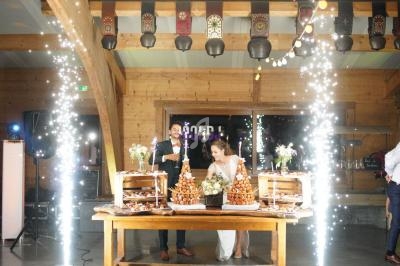 Un couple coupe une pièce montée entourée de décorations lumineuses dans une salle en bois.