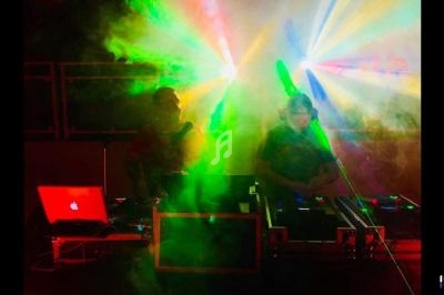 Deux DJ mixant sur scène avec des lumières colorées et de la fumée créant une ambiance festive.