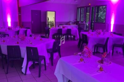 Salle de réception décorée avec des tables dressées, éclairage violet et chaises noires.