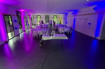 Salle décorée avec des lumières violettes et bleues, tables dressées pour un événement, avec quelques personnes au fond.