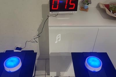 Deux dispositifs lumineux bleus sur des supports noirs, avec un chronomètre affichant ’015’ en arrière-plan.