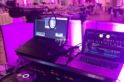 Poste de DJ avec platines, ordinateurs et micros, installé dans une salle de réception décorée avec des lumières roses.