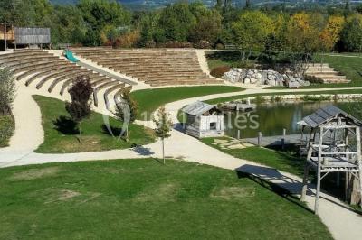 Un artiste sur échasses interagit avec une femme dans un espace intérieur éclairé, avec des spectateurs en arrière-plan.