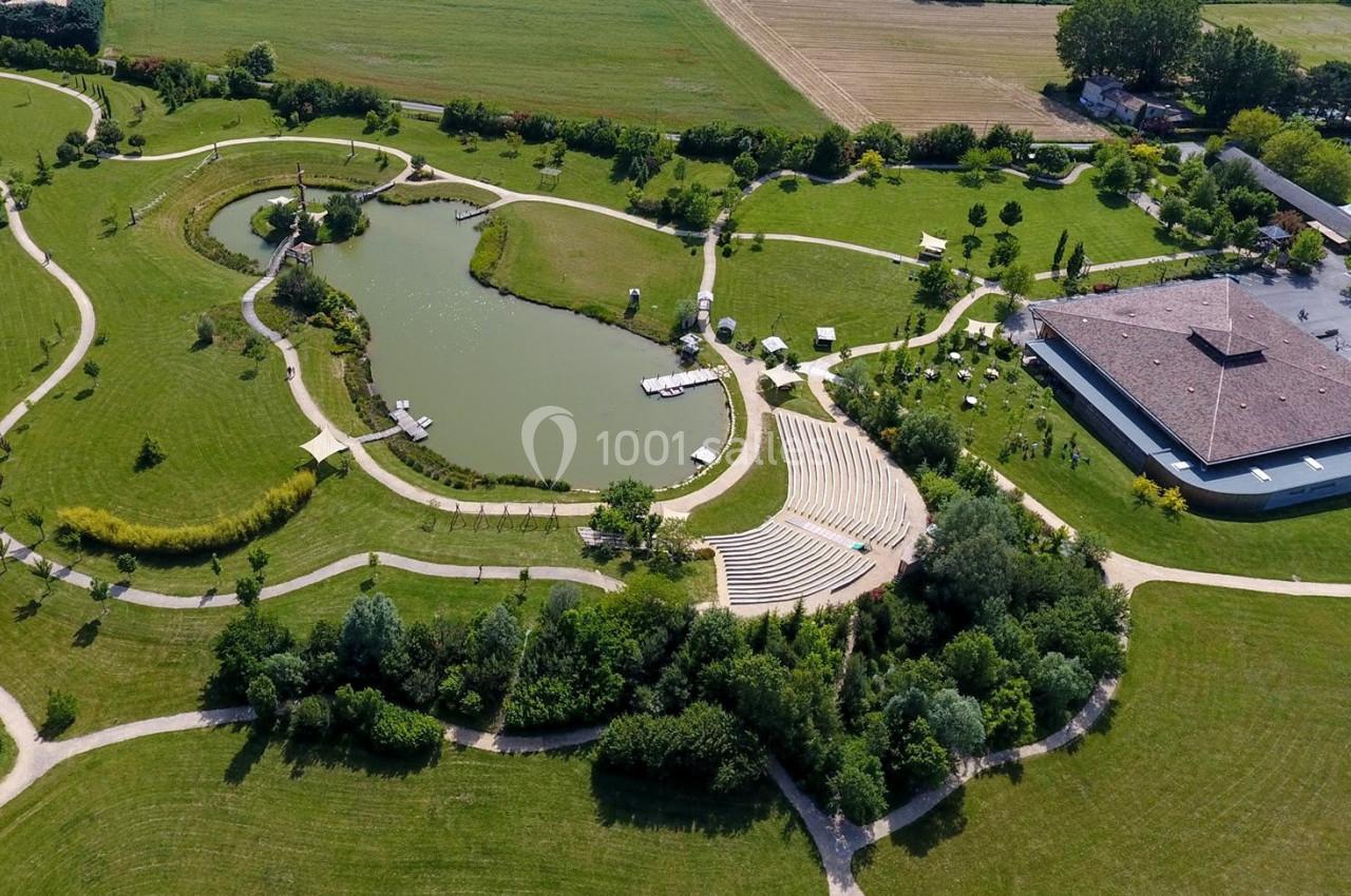 Vue aérienne d'un parc avec un étang, des chemins sinueux, un amphithéâtre en plein air et un bâtiment adjacent.