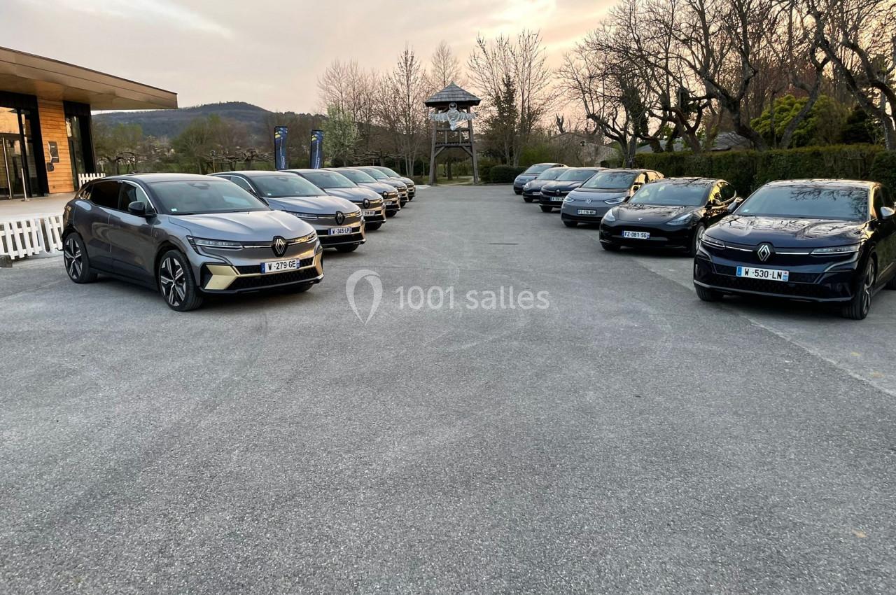 Alignement de voitures électriques garées sur un parking extérieur au crépuscule, entouré d'arbres et de bâtiments.