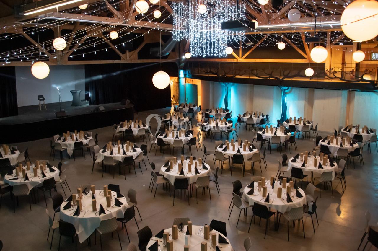 Salle de réception décorée avec des tables rondes dressées, éclairage tamisé et guirlandes lumineuses suspendues.