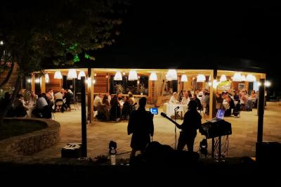 Un artiste sur échasses interagit avec une femme dans un espace intérieur éclairé, avec des spectateurs en arrière-plan.