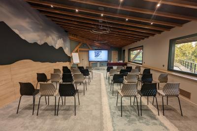 Un artiste sur échasses interagit avec une femme dans un espace intérieur éclairé, avec des spectateurs en arrière-plan.