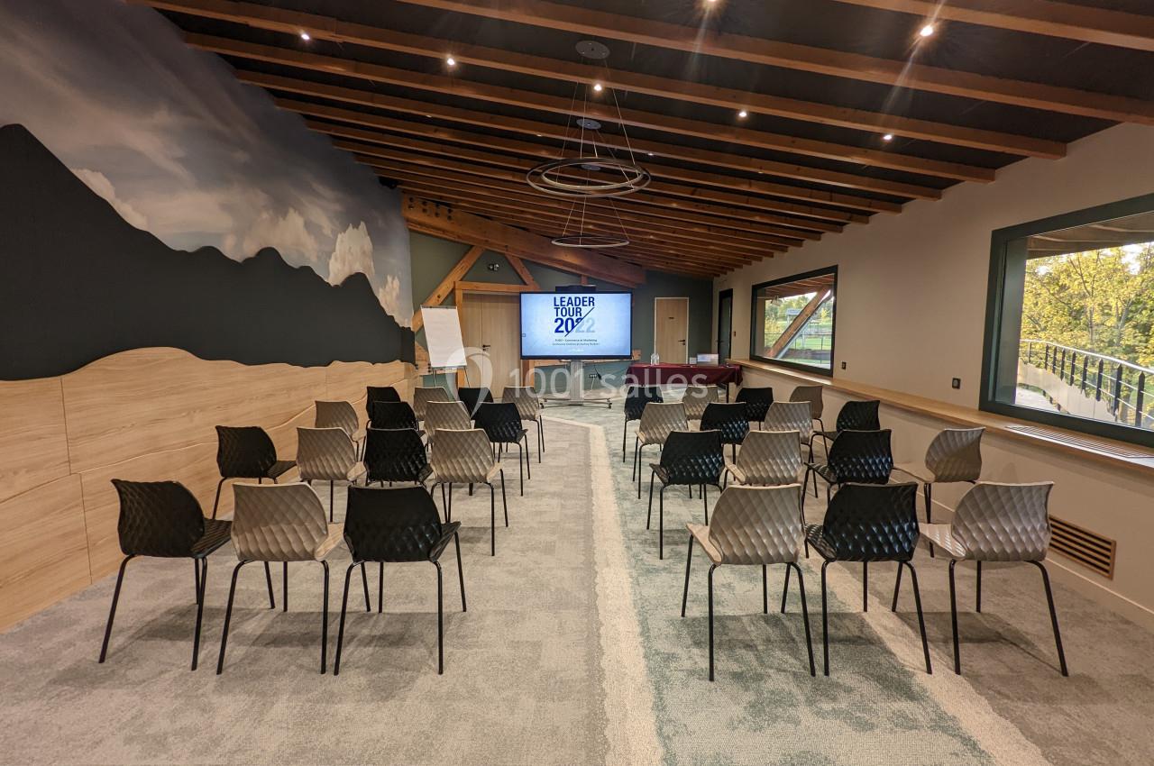 Salle de conférence lumineuse avec des rangées de chaises vides, un écran de présentation et un mur décoré de montagnes.
