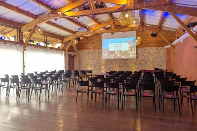 Un artiste sur échasses interagit avec une femme dans un espace intérieur éclairé, avec des spectateurs en arrière-plan.