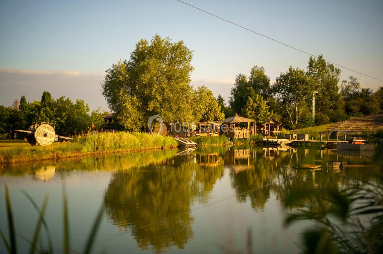 Plan d'eau calme entouré de végétation, avec des cabanes en bois et un bateau échoué sur la rive.