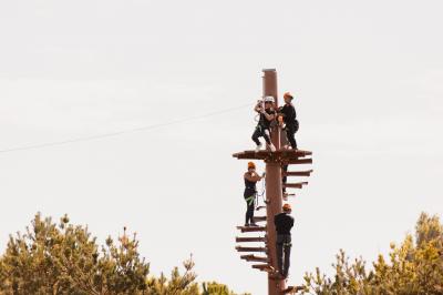 Un artiste sur échasses interagit avec une femme dans un espace intérieur éclairé, avec des spectateurs en arrière-plan.