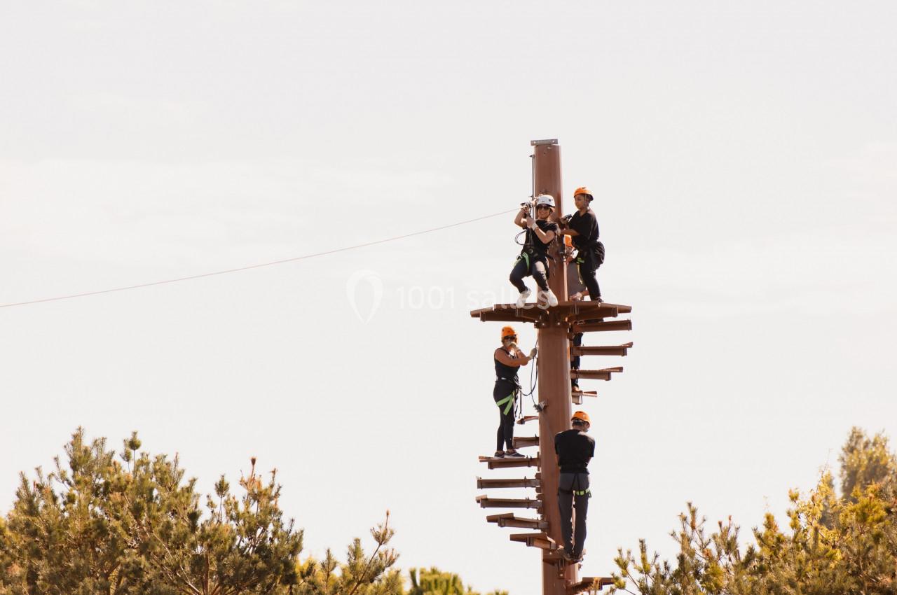 Des personnes équipées de harnais escaladent une structure en bois dans un parcours d'accrobranche en plein air.