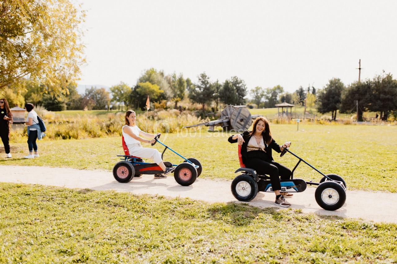 Deux personnes conduisent des karts à pédales sur un chemin dans un parc par une journée ensoleillée.