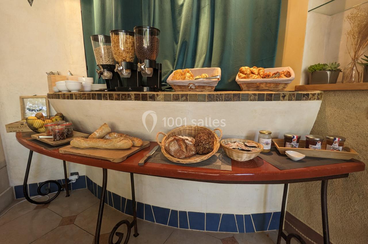Buffet de petit-déjeuner avec pains, viennoiseries, confitures, céréales et fruits disposés sur une table en bois.
