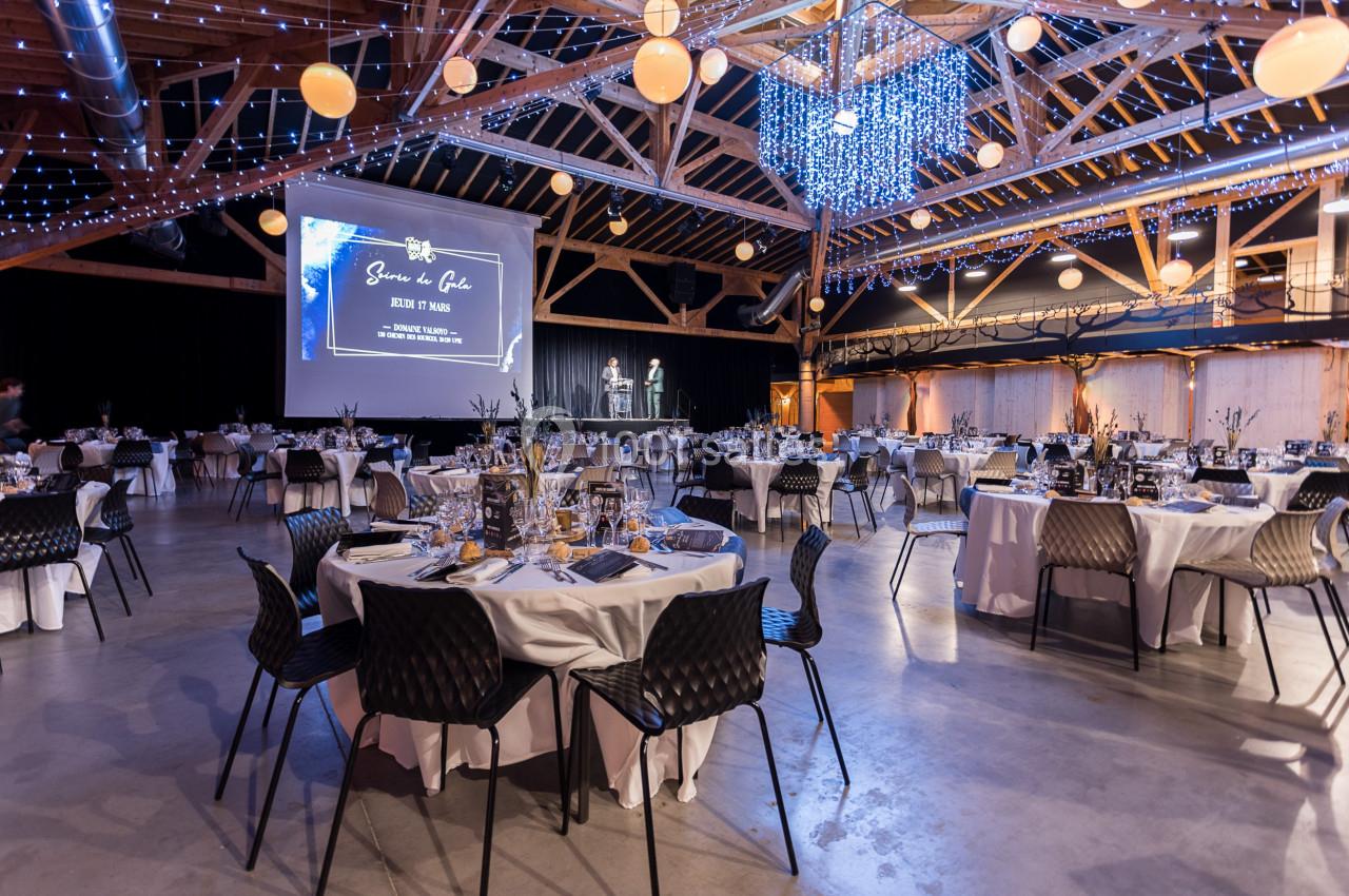 Salle de réception décorée avec des tables dressées, des guirlandes lumineuses et un écran de projection.