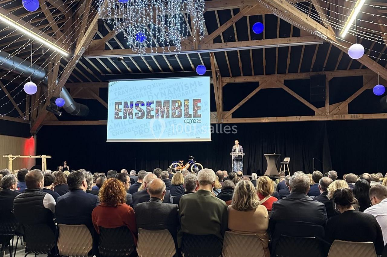 Salle de conférence avec un public assis, un orateur sur scène et un écran affichant le mot ’ENSEMBLE’.