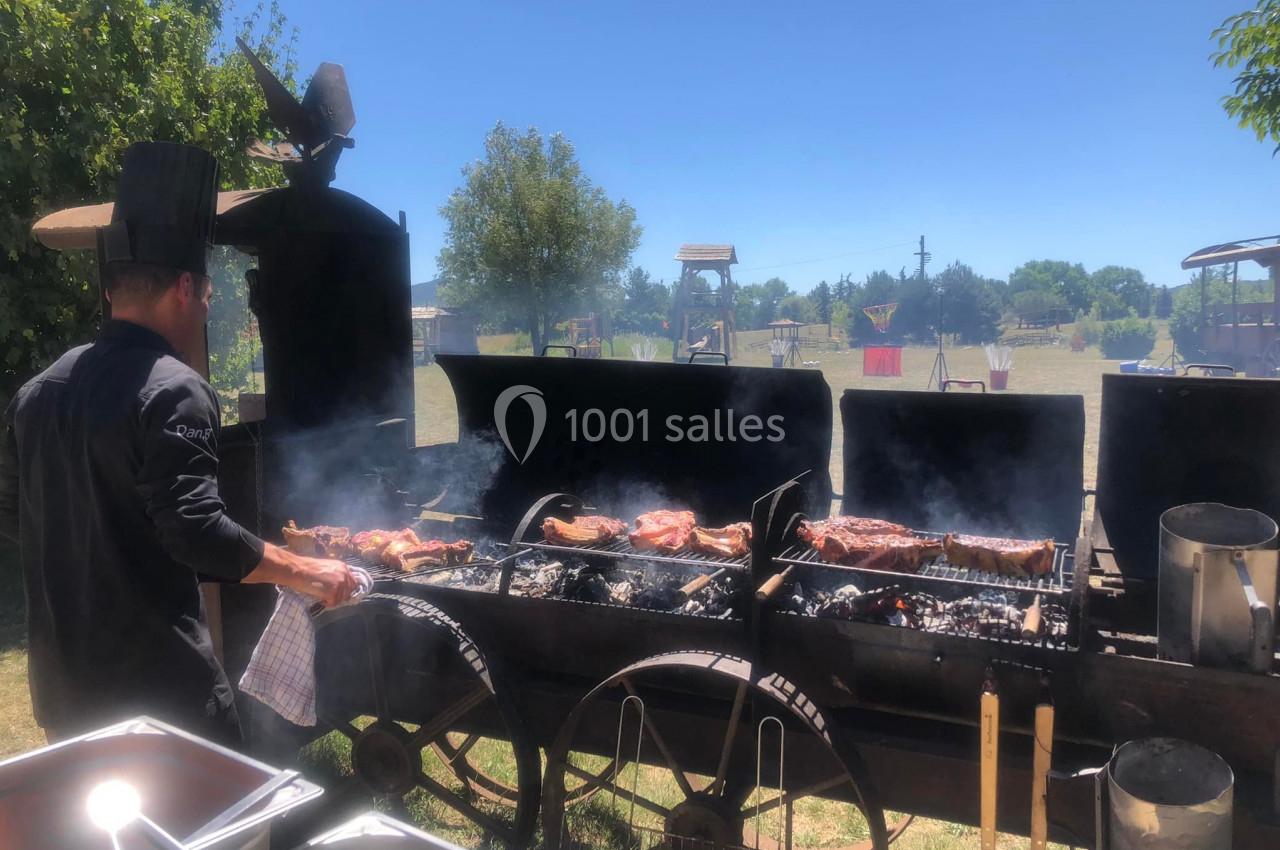 Un cuisinier prépare des viandes grillées sur un grand barbecue en plein air, par une journée ensoleillée.