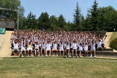 Un artiste sur échasses interagit avec une femme dans un espace intérieur éclairé, avec des spectateurs en arrière-plan.