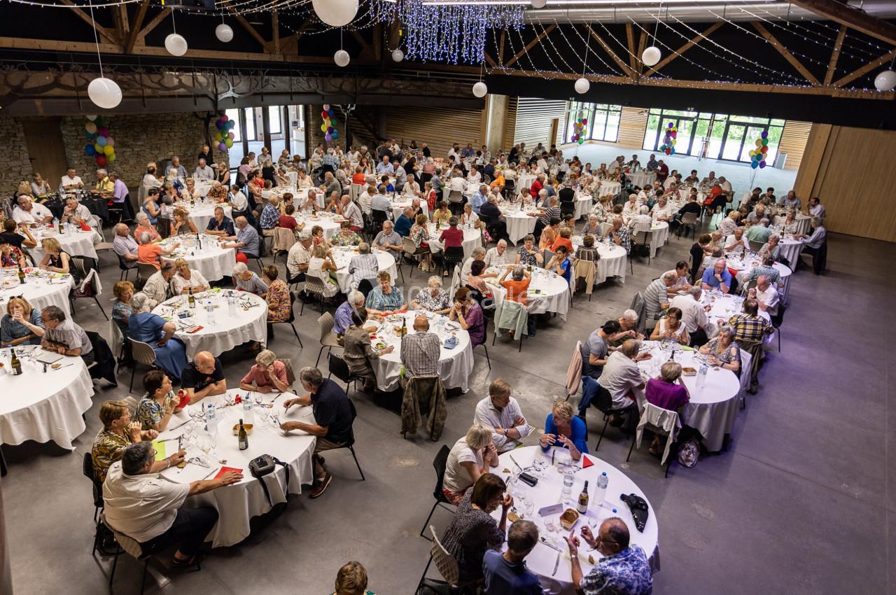 Salle de réception remplie de convives assis à des tables rondes, décorée de guirlandes lumineuses et de ballons.