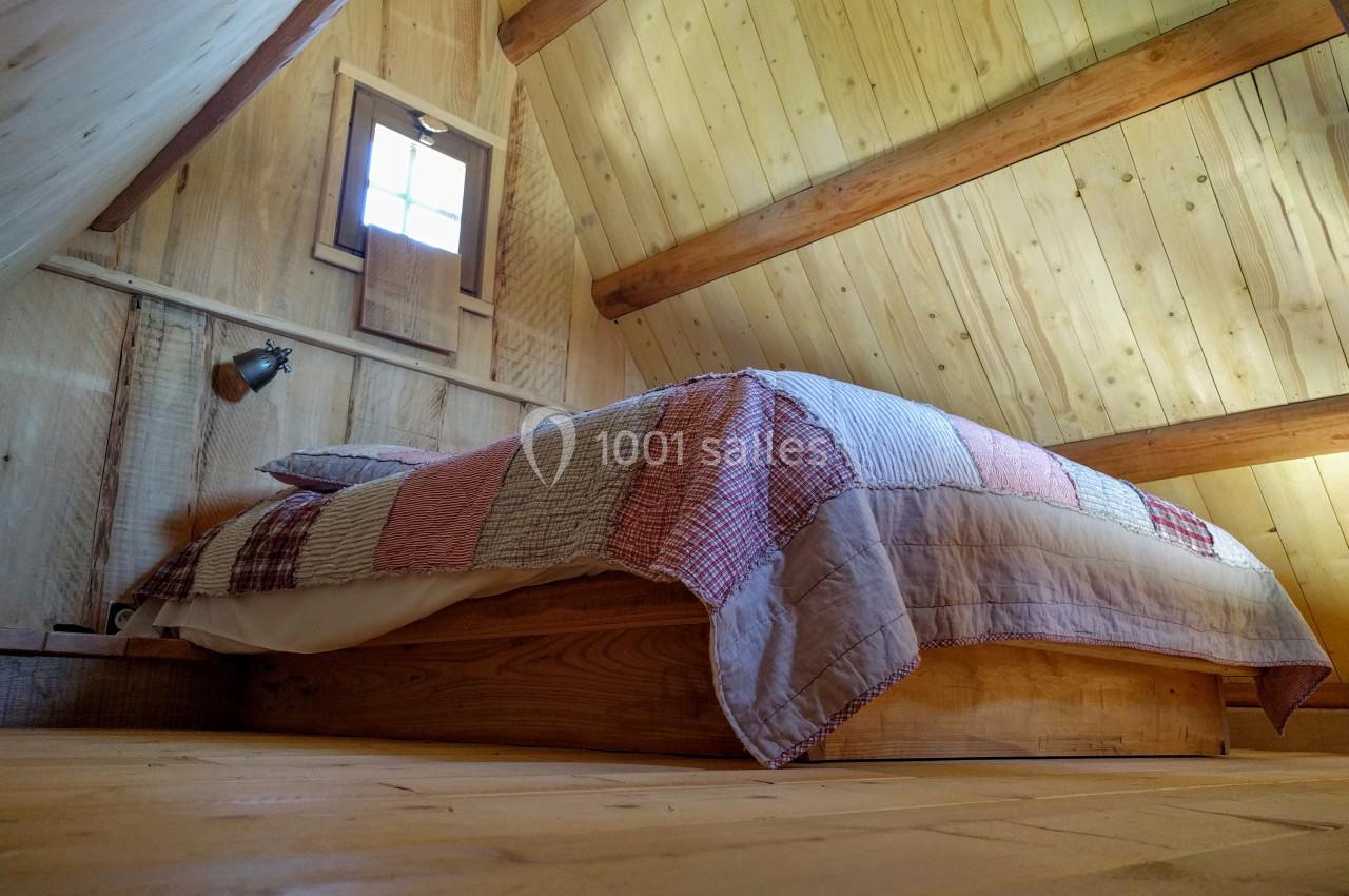 Lit en bois avec une couverture à motifs dans une chambre mansardée aux murs et plafond en bois clair.