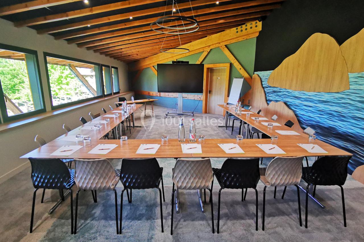 Salle de réunion lumineuse avec grande table en U, chaises modernes, écran, et décor mural évoquant la nature.