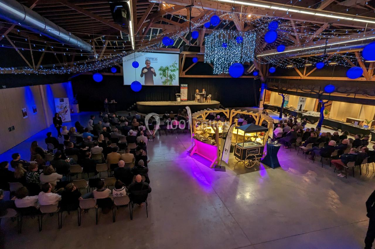 Salle de conférence avec un public assis, une présentation sur scène et des décorations lumineuses suspendues.