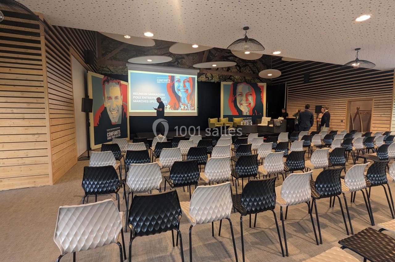 Salle de conférence vide avec des rangées de chaises, un écran de présentation et des affiches sur scène.