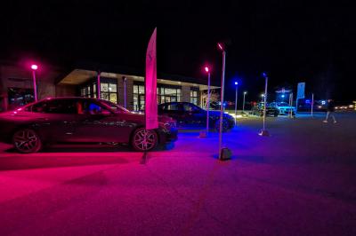 Un artiste sur échasses interagit avec une femme dans un espace intérieur éclairé, avec des spectateurs en arrière-plan.