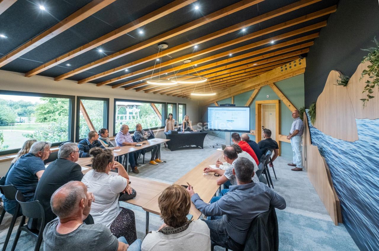 Un groupe de personnes assises dans une salle de réunion lumineuse, écoutant une présentation sur écran.