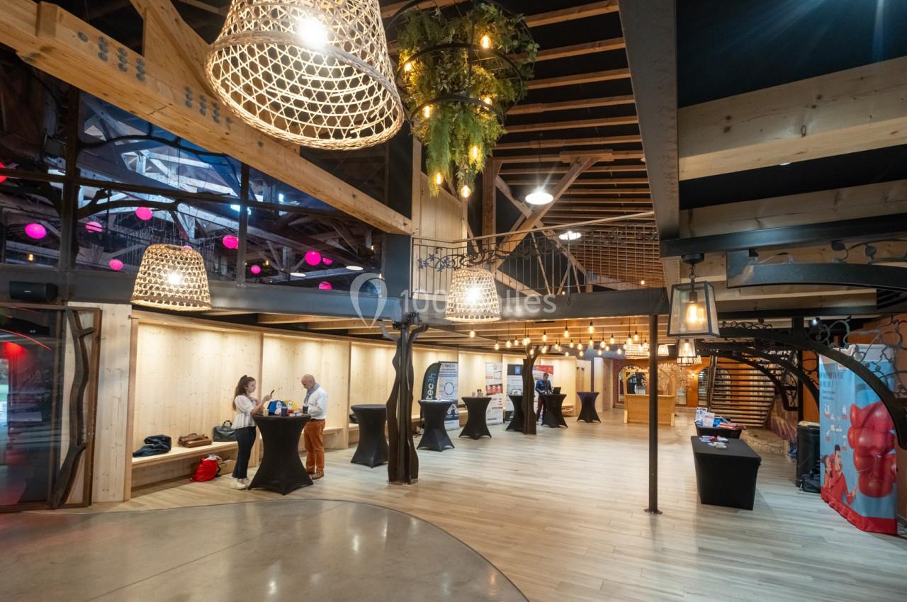 Intérieur d'un espace événementiel avec des stands, des luminaires suspendus et un décor en bois.