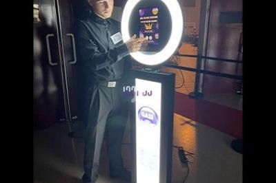 Un homme en tenue formelle utilise une borne photo équipée d'un anneau lumineux dans un espace intérieur.