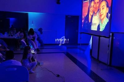 Projection d'une photo de famille sur un écran dans une salle éclairée par des lumières bleues, avec des spectateurs assis.