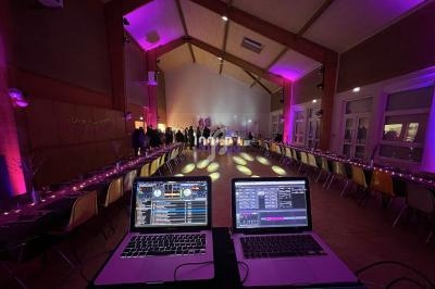 Salle de réception éclairée en lumière violette avec des tables dressées et une régie DJ au premier plan.