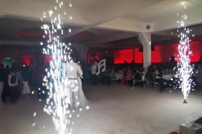 Un couple danse au centre d'une salle éclairée de rouge, entouré de fumée et de fontaines d'étincelles.